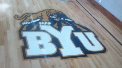 Close-up of dark hardwood flooring with white BYU Cougar logo inlay featuring the letter 'Y' and a cougar head design