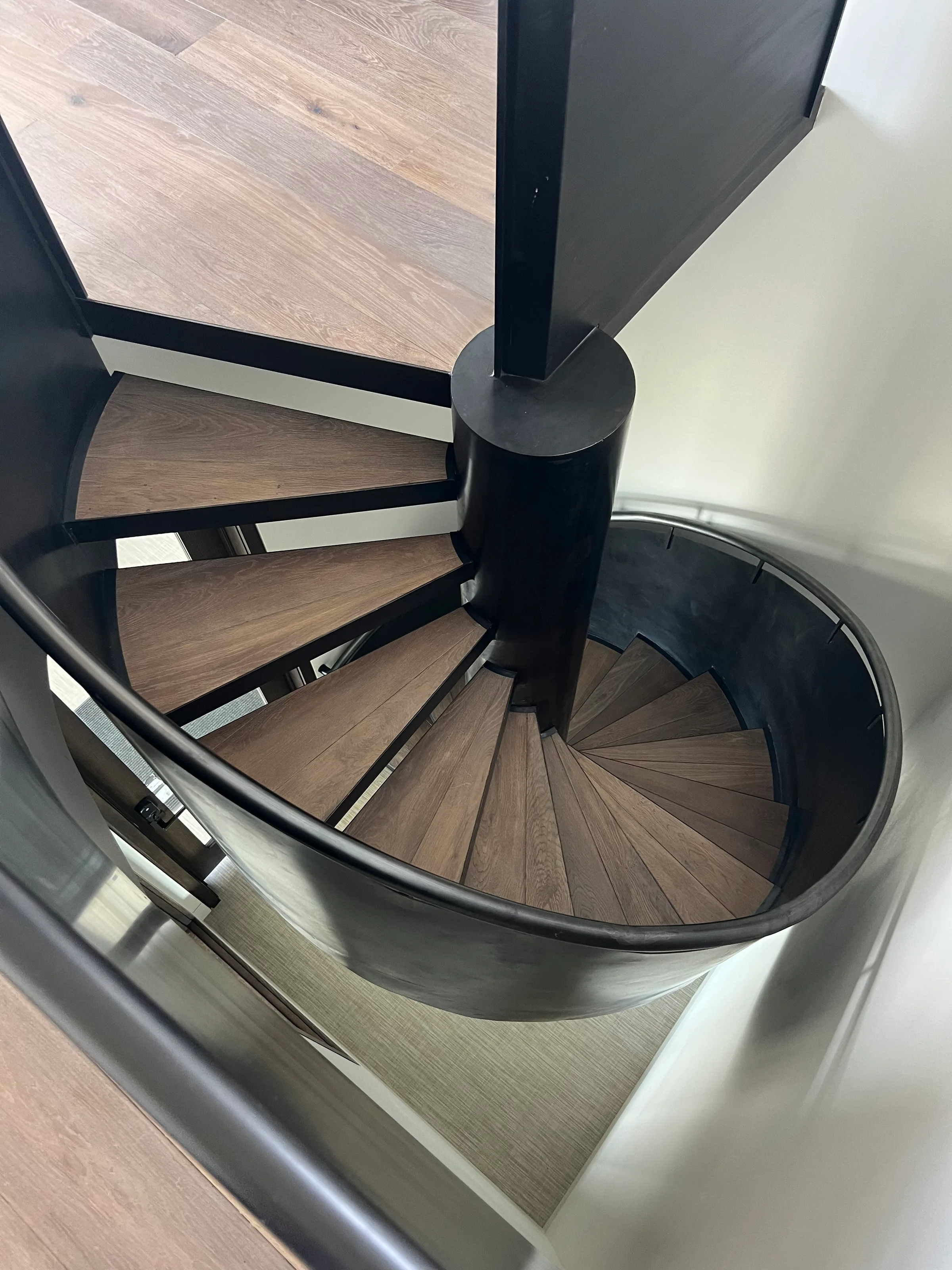 Pre-finished light wood spiral staircase with pie-shaped treads and curved metal railings