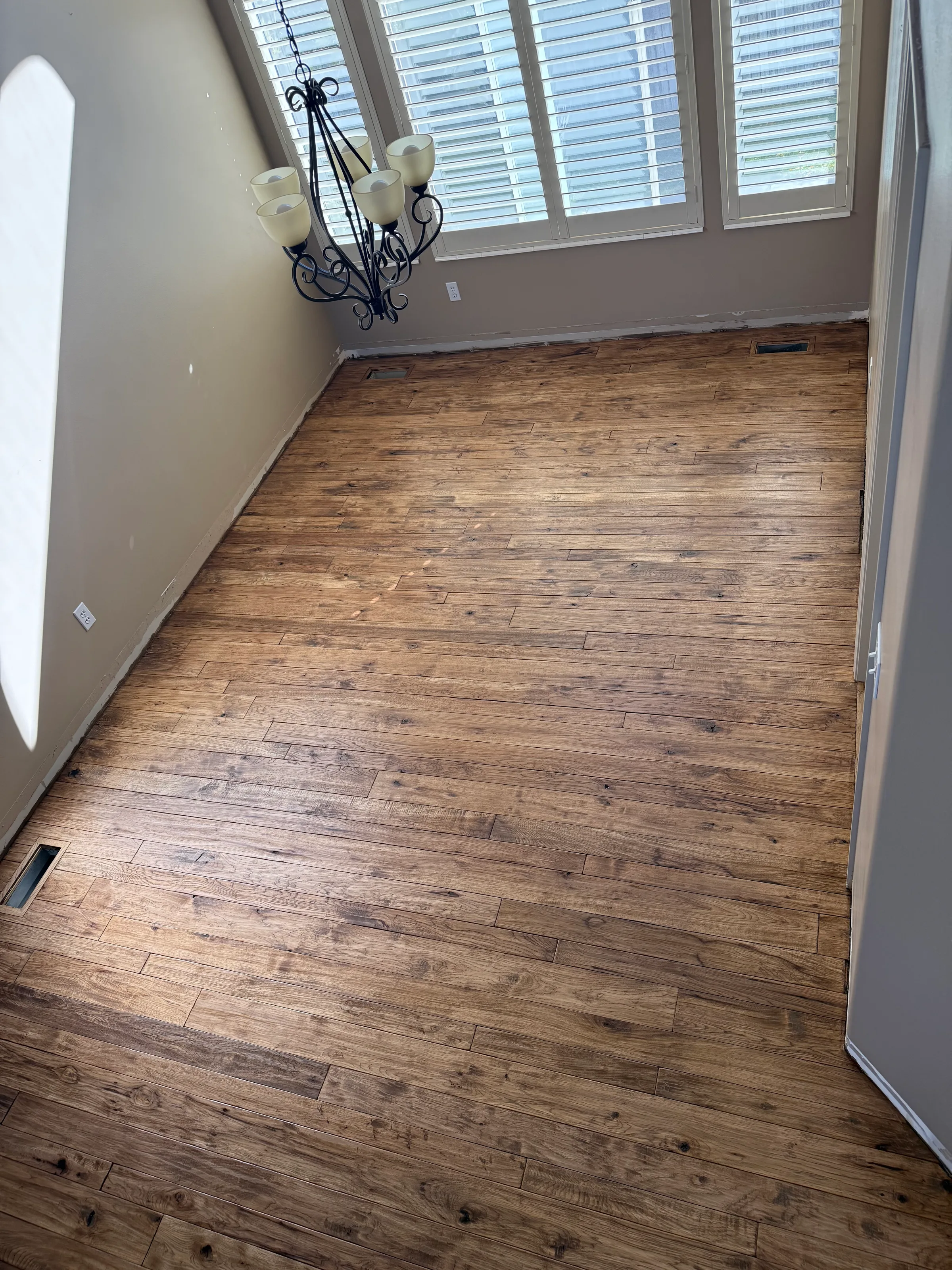 Refinished hand-scraped hickory hardwood flooring with warm medium-brown tone and visible texture marks throughout a residential room.