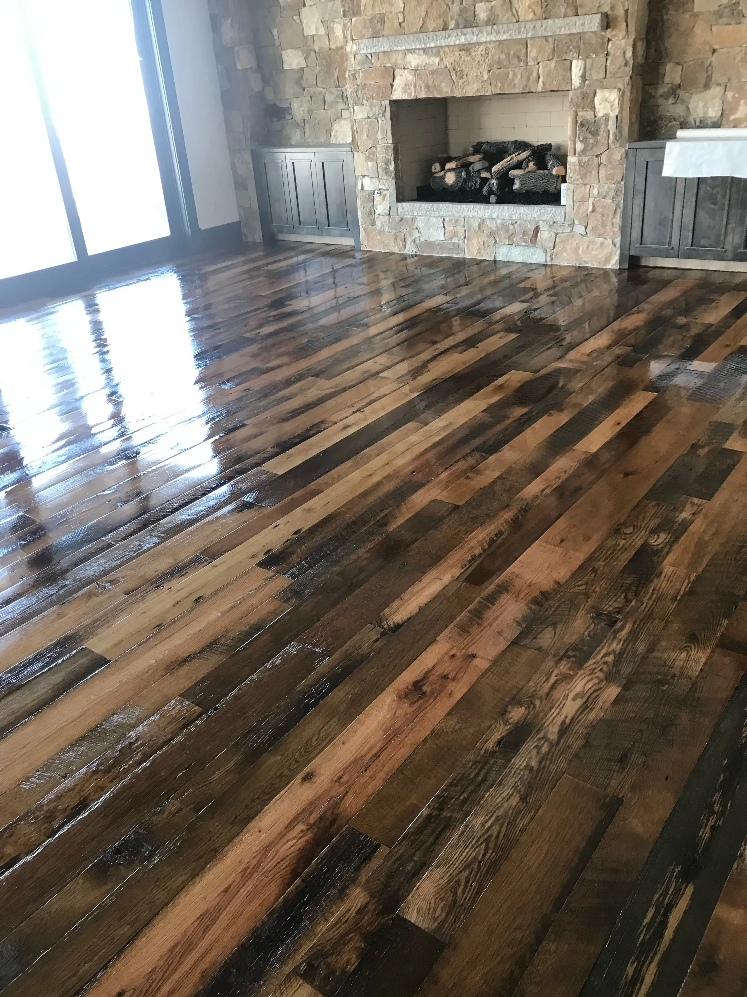 Warm-toned reclaimed oak hardwood flooring with rich grain character and varied patina, lit by dramatic diagonal window shadows.