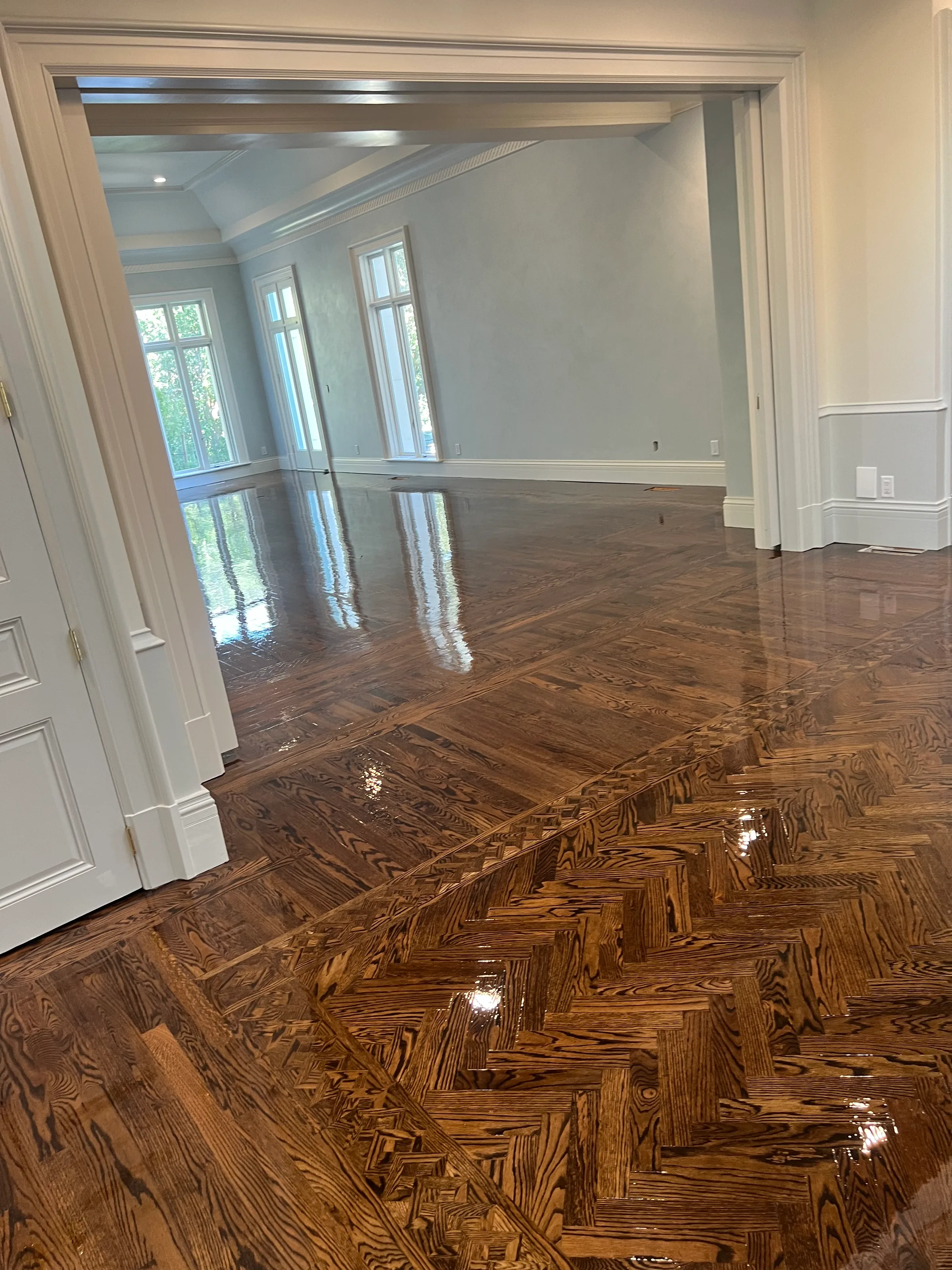 Red oak flooring in herringbone pattern with geometric border inlay in bright residential entry