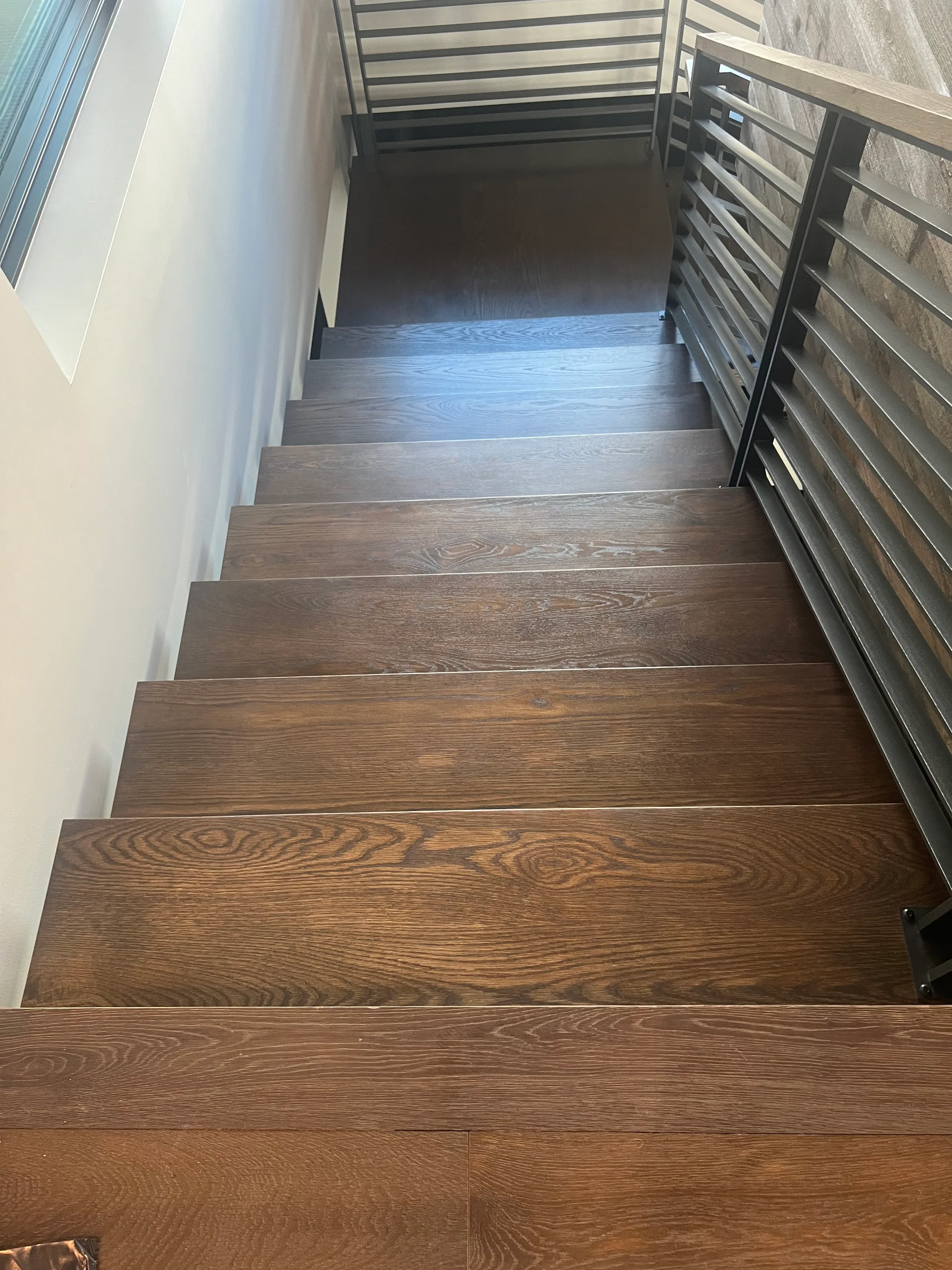 White oak floating staircase with cantilevered treads and black steel support frame, natural light from windows
