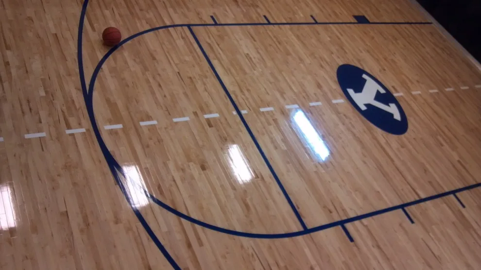 Close-up of dark hardwood flooring with white BYU Cougar logo inlay featuring the letter 'Y' and a cougar head design