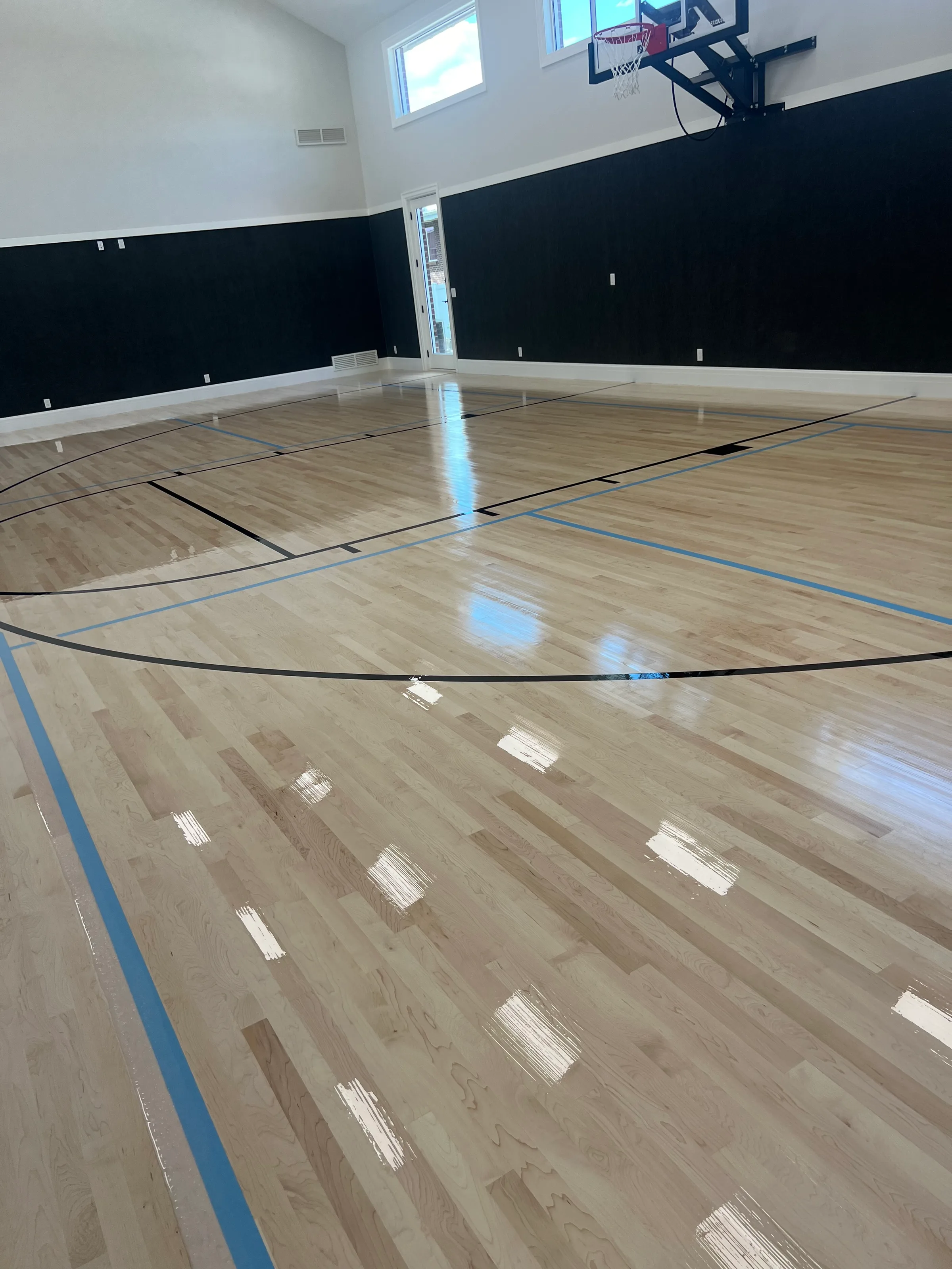 Light-toned wood sport floor with linear grain pattern illuminated by overhead lighting in gymnasium