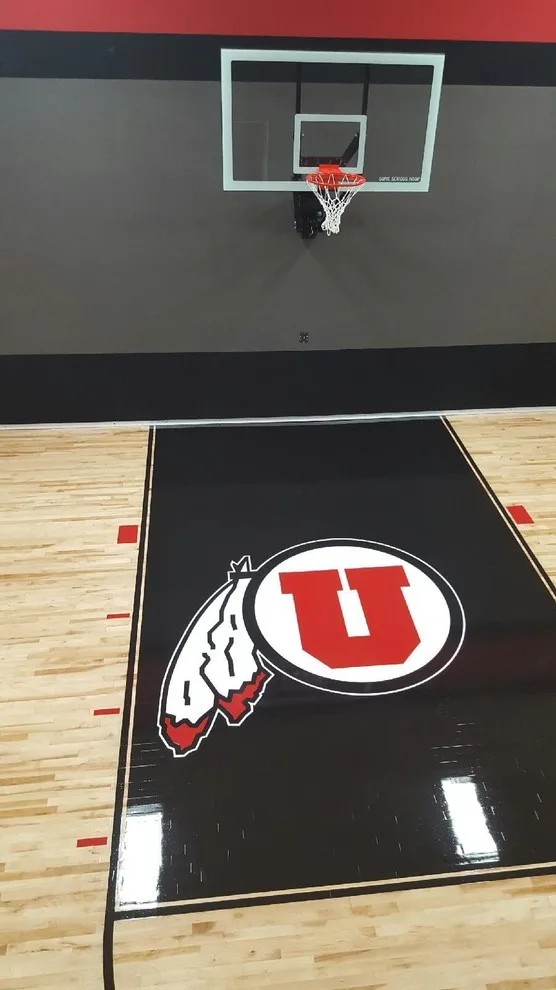 Basketball court featuring light maple flooring with dark bordered Utah Utes custom logo inlay and painted boundary lines