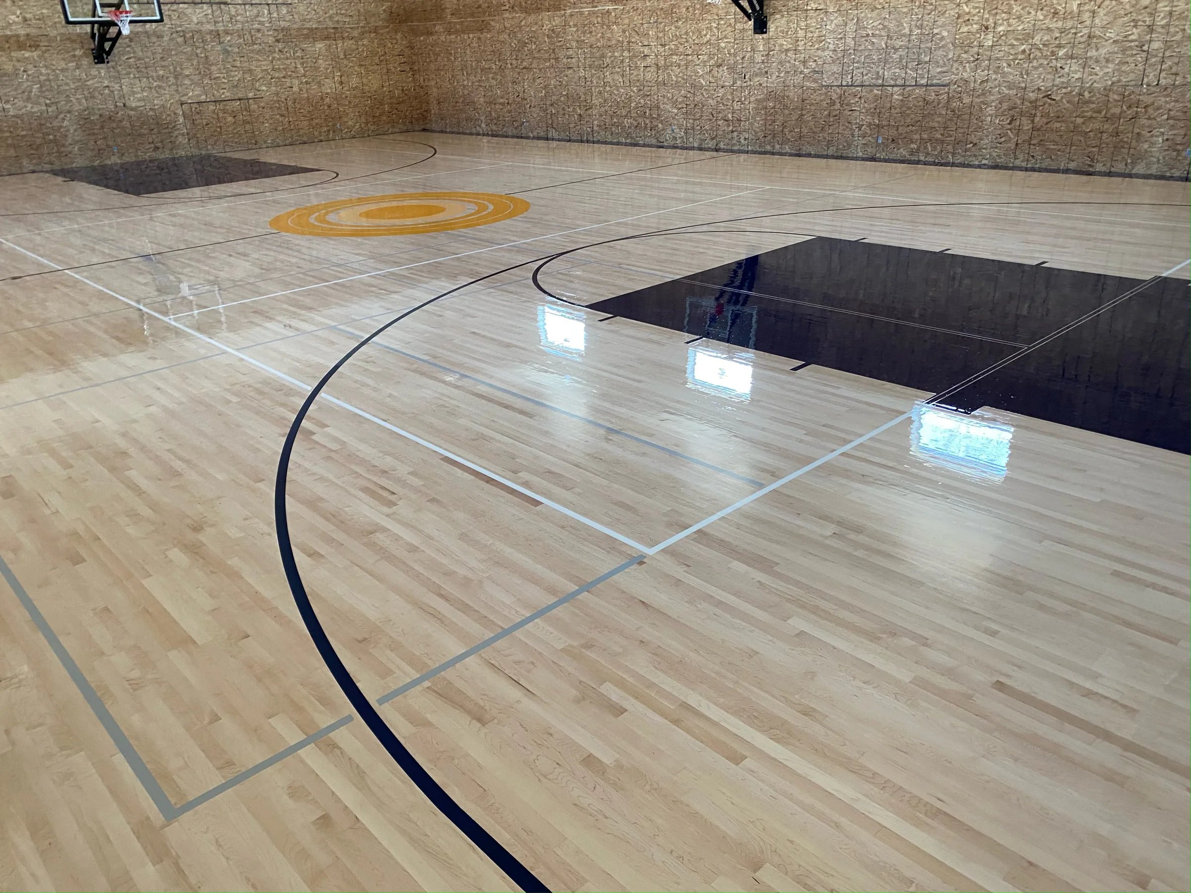 Newly installed light wood basketball court floor with center court logo, court lines, and dehumidification equipment visible.