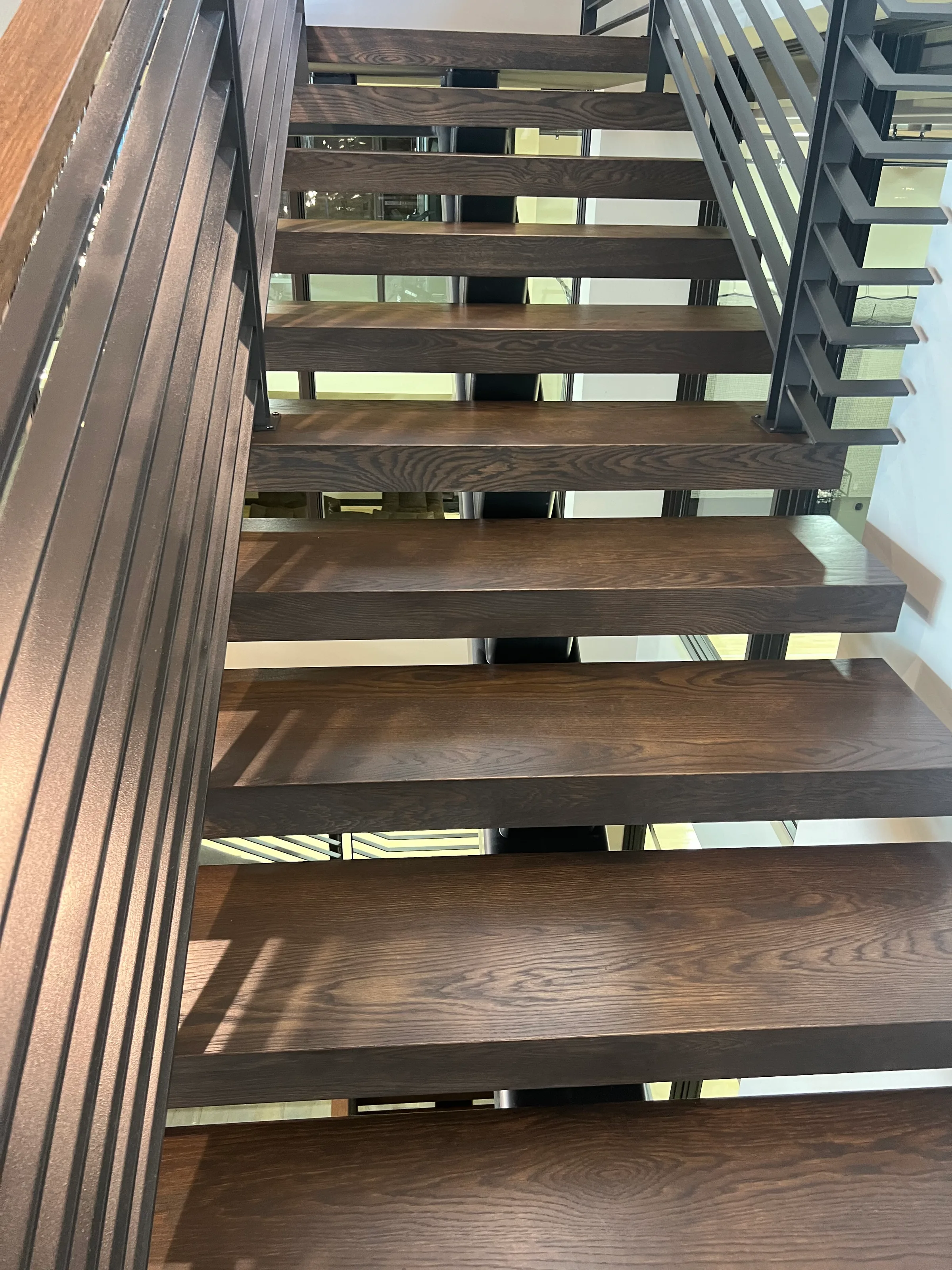 Custom white oak staircase with suspended treads and open steel frame, bright natural light from large windows