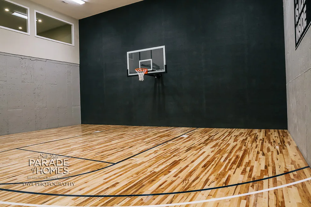 Rectangular basketball court with maple hardwood flooring, navy painted boundary lines, white center circle, and basketball hoop mounted on wall